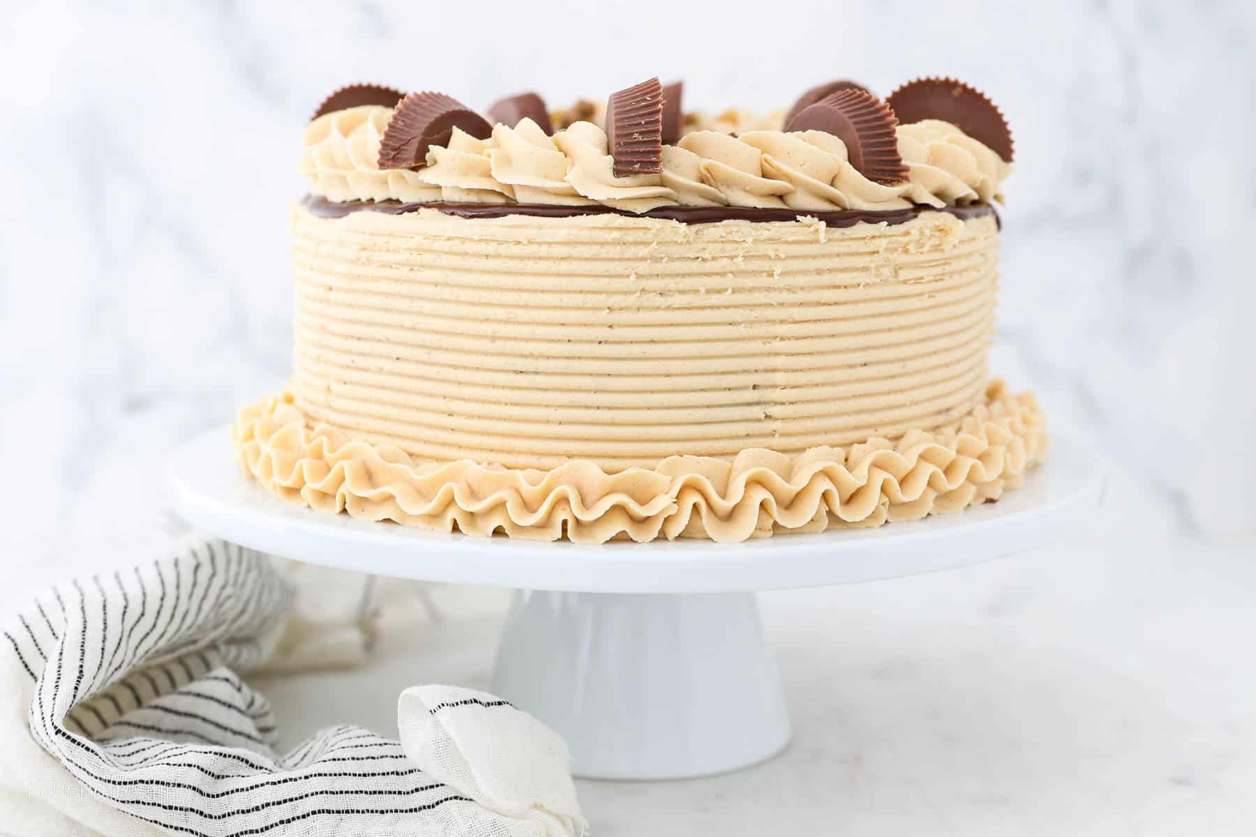 Frosted chocolate peanut butter layer cake on a white cake stand.