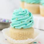 An unwrapped vanilla cupcake with teal frosting and sprinkles