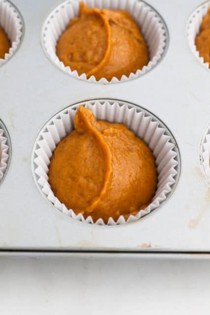 Pumpkin muffin batter in the tin with a cupcake liner.