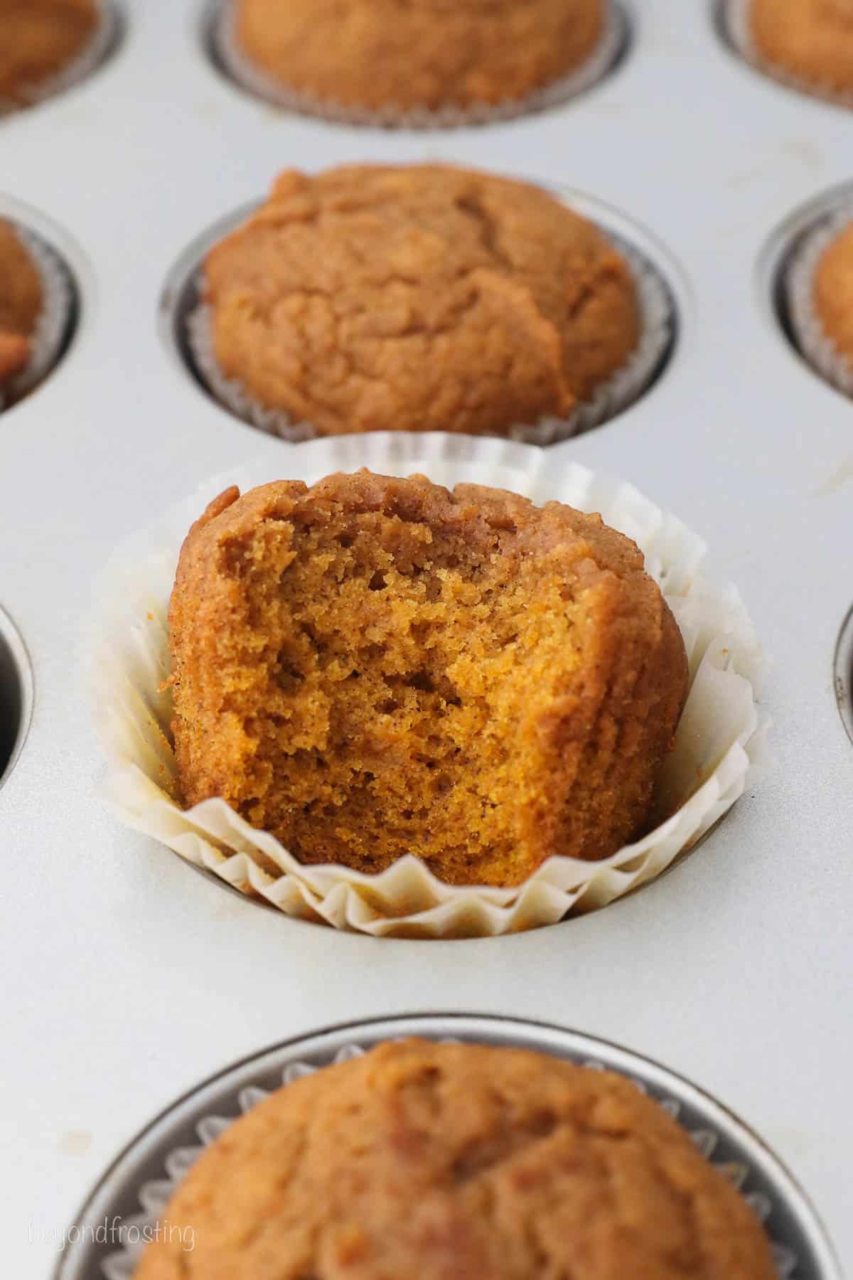 a muffins pan with pumpkin muffins, one has a bite missing