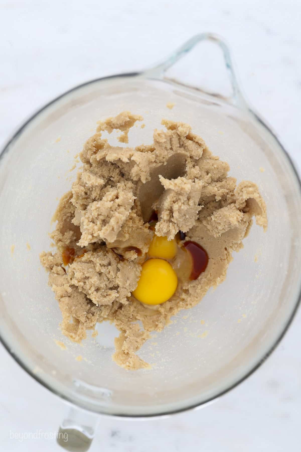 Eggs and vanilla added to cookie dough in a glass bowl.