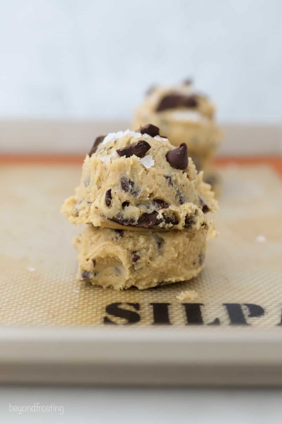 Two scoops of cookie dough on top of one another on a silpat lined baking sheet.