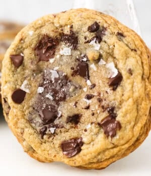 Close up of a giant chocolate chip cookie leaning against a glass of milk.