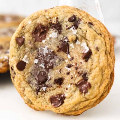Close up of a giant chocolate chip cookie leaning against a glass of milk.