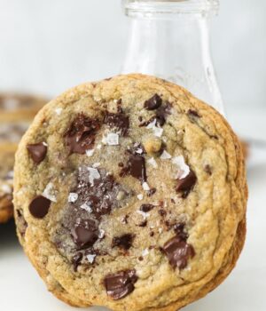 A chocolate chip cookie leaning up against a milk glass