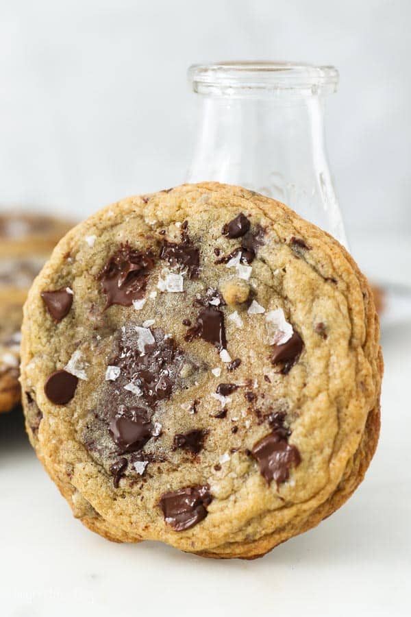 A chocolate chip cookie leaning up against a milk glass