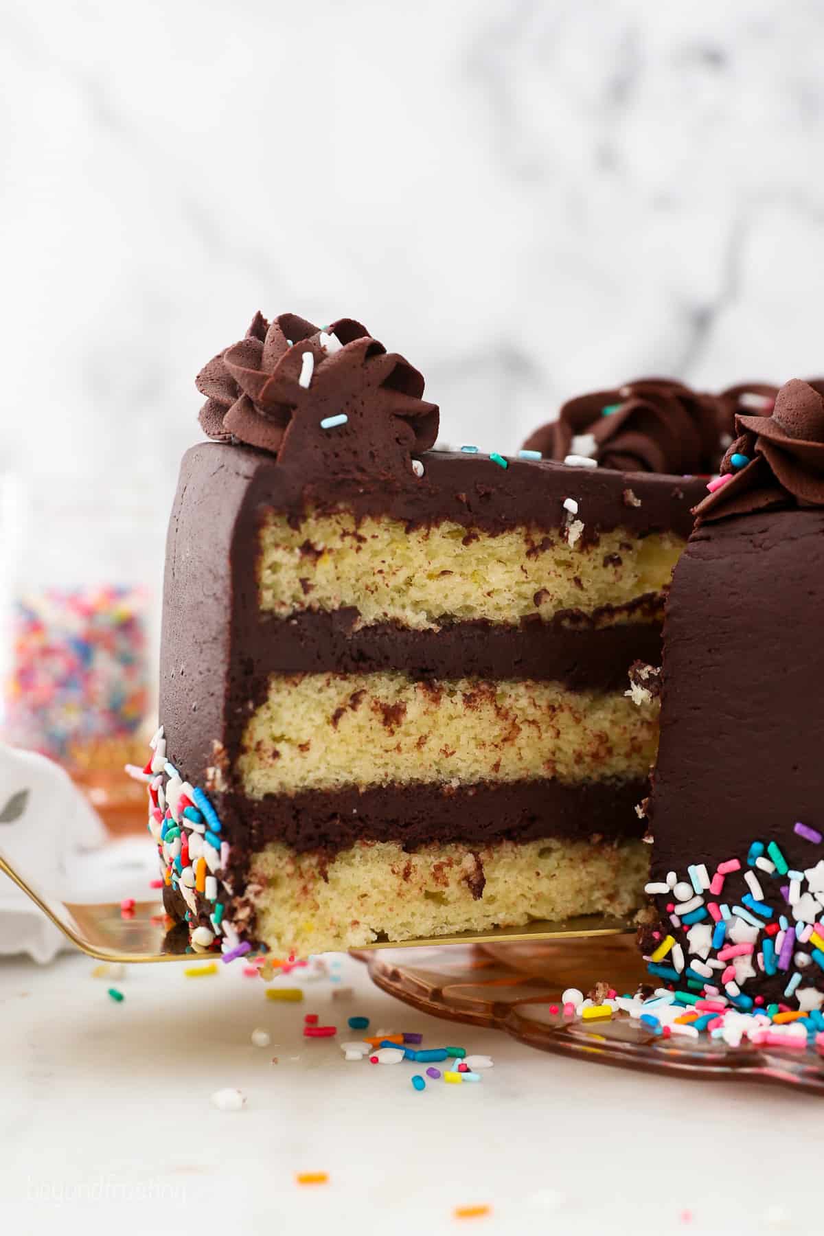 A slice of yellow layer cake with chocolate frosting being lifted from the rest of the cake.