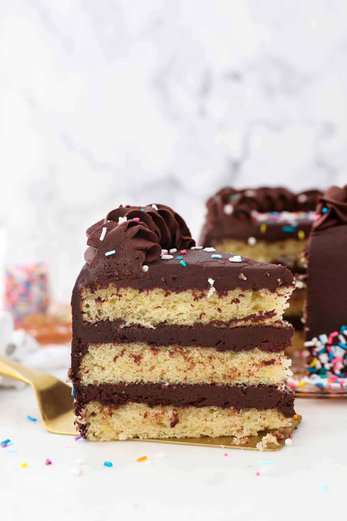 A slice of yellow layer cake with chocolate frosting.