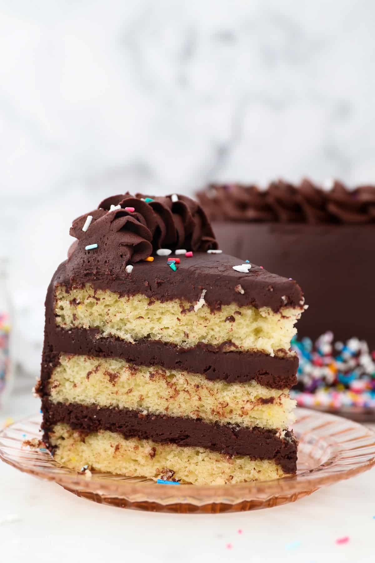 A slice of yellow layer cake with chocolate frosting.