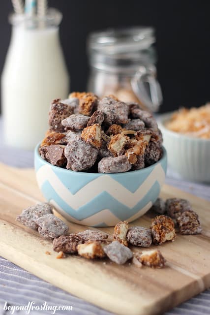 A Bowl of Samoa Muddy Buddies on a Cutting Board Beside a Glass of Milk