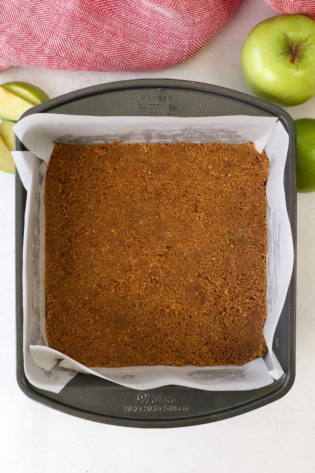 Cheesecake crust pressed into the bottom of a lined square pan.