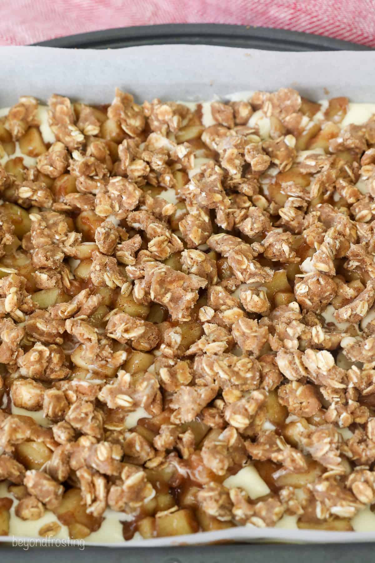 Overhead view of the crumble topping on apple cheesecake bars in a baking pan.