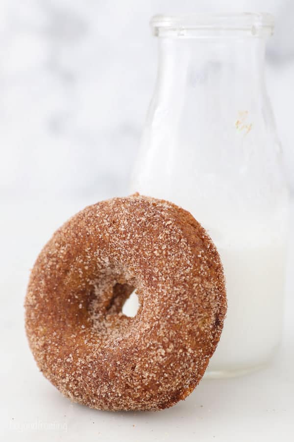 A pumpkin donut leaning up against a glass of milk