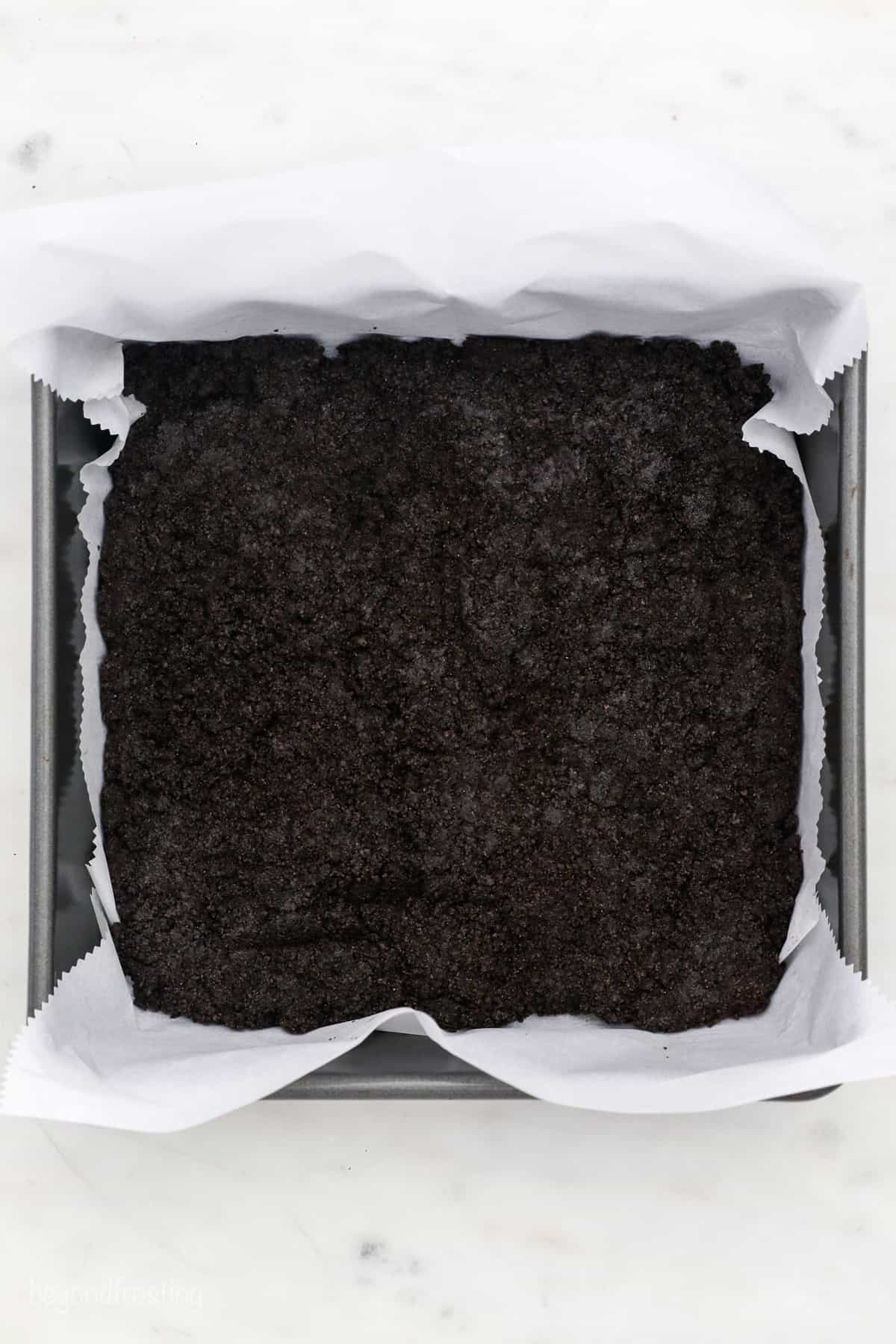 Oreo crust pressed into the bottom of a square baking pan lined with parchment paper.