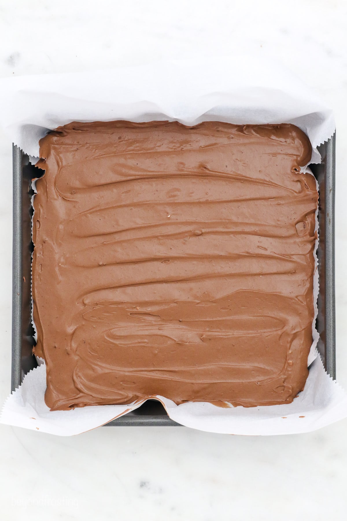 Unbaked chocolate cheesecake inside a square baking pan lined with parchment paper.