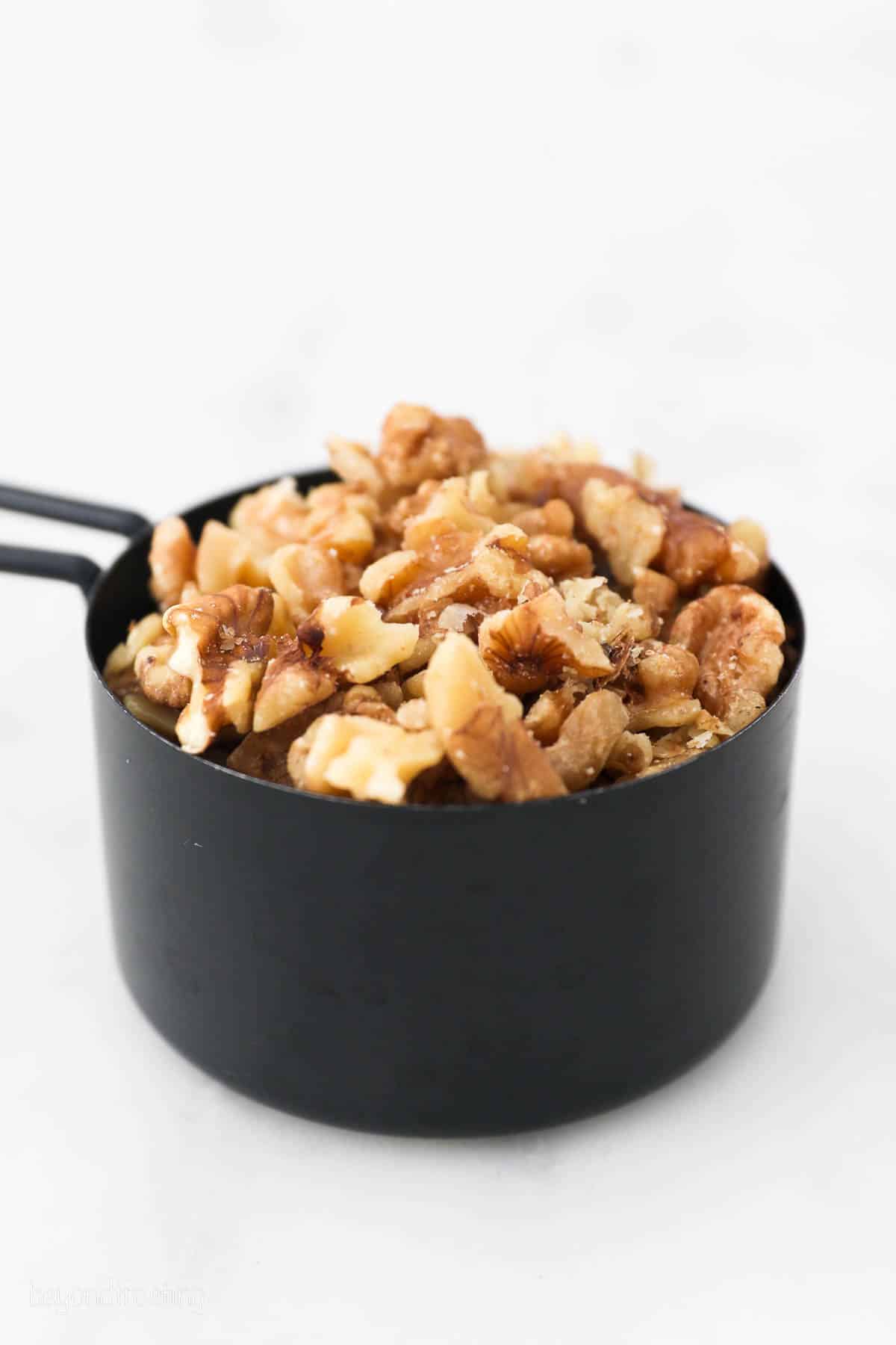 A black measuring cup filled with walnuts.
