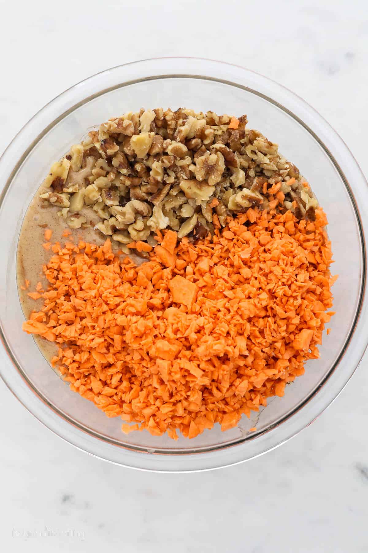 Shredded sweet potato and chopped walnuts added to sweet potato cake batter in a glass mixing bowl.