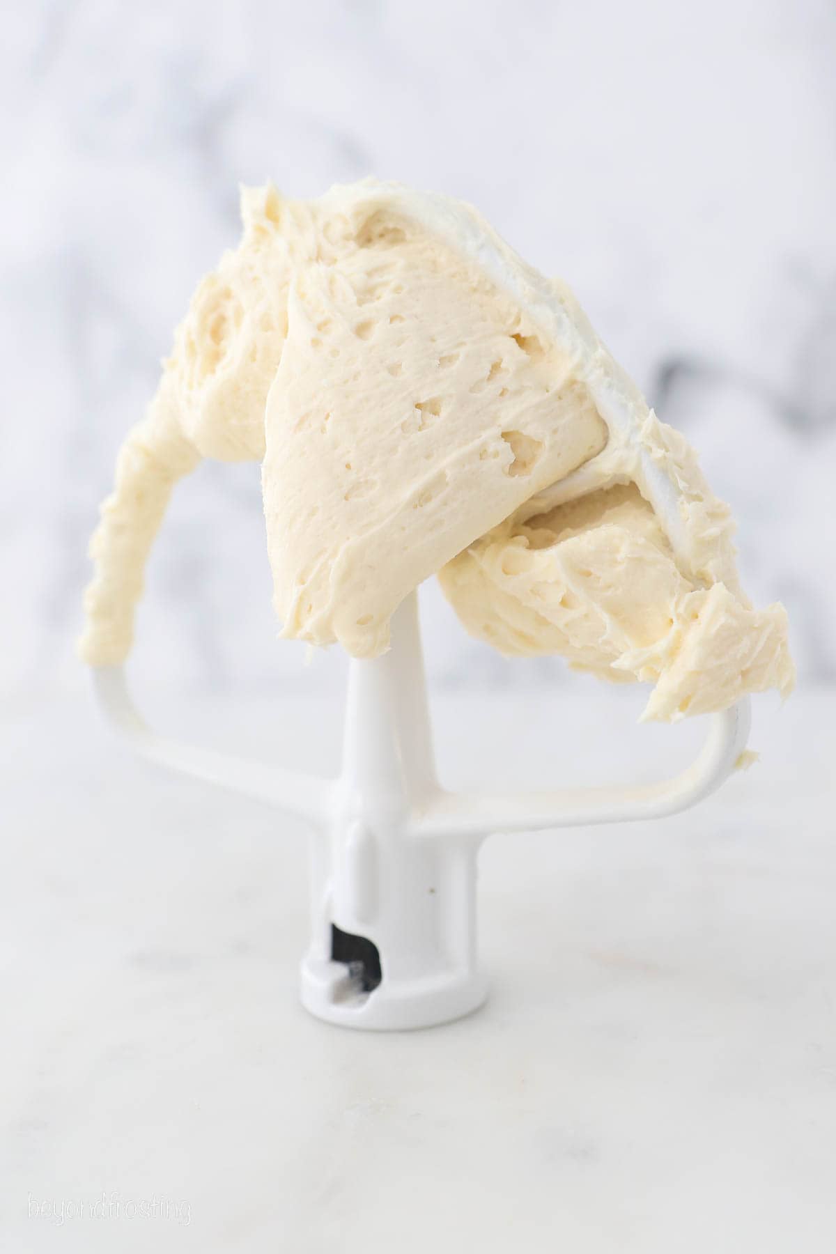 A stand mixer attachment covered with bourbon salted caramel frosting standing upright on a marble countertop.