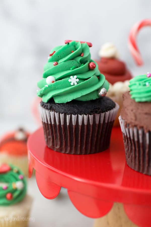 A Christmas tree cupcake on a red cake stand