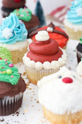 Assorted Christmas cupcakes decorated with buttercream Christmas trees, Santa, and reindeer.