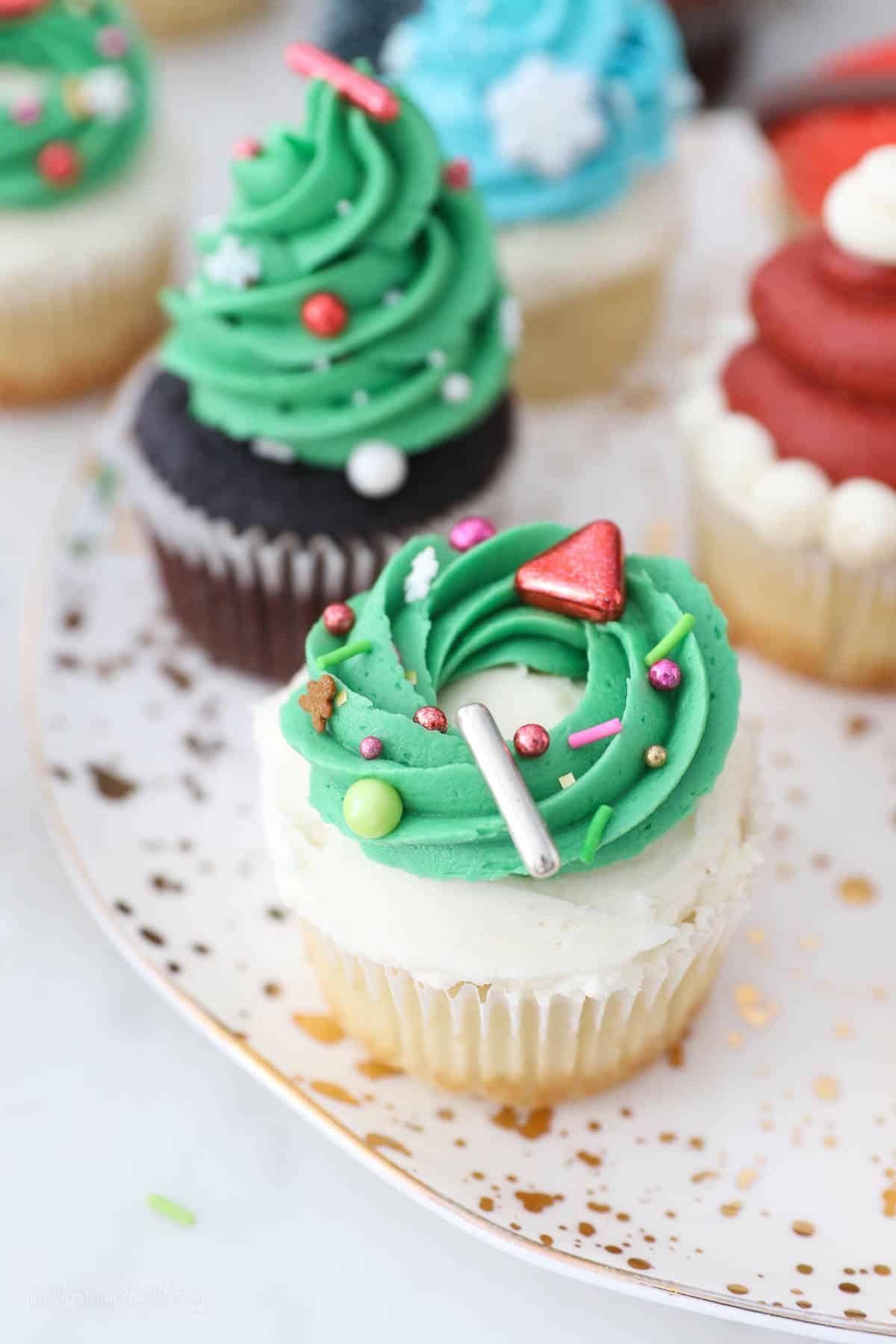 Assorted Christmas cupcakes decorated with a buttercream Christmas tree and a wreath with sprinkles.