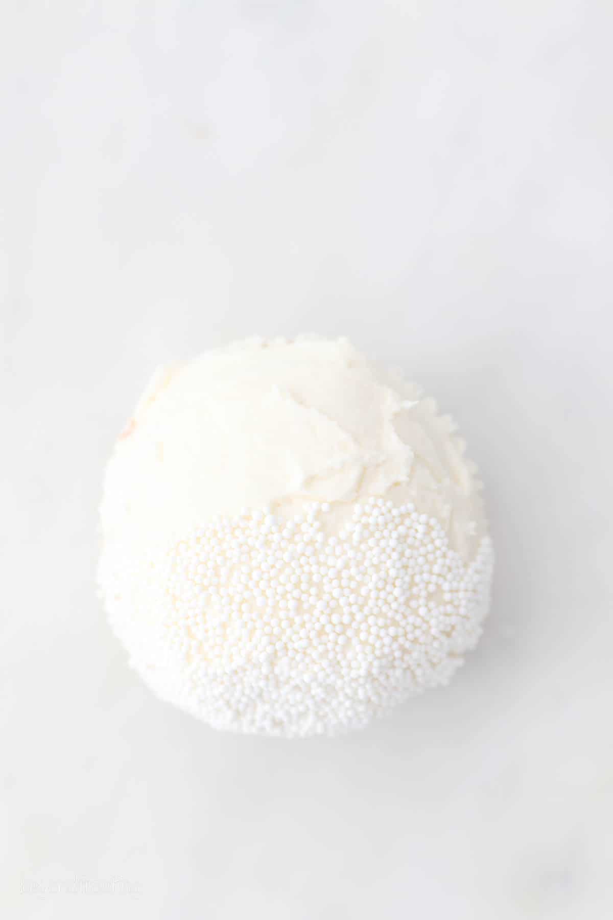 Overhead view of a cupcake frosted with white buttercream, with the bottom third covered in a white sprinkle "beard".