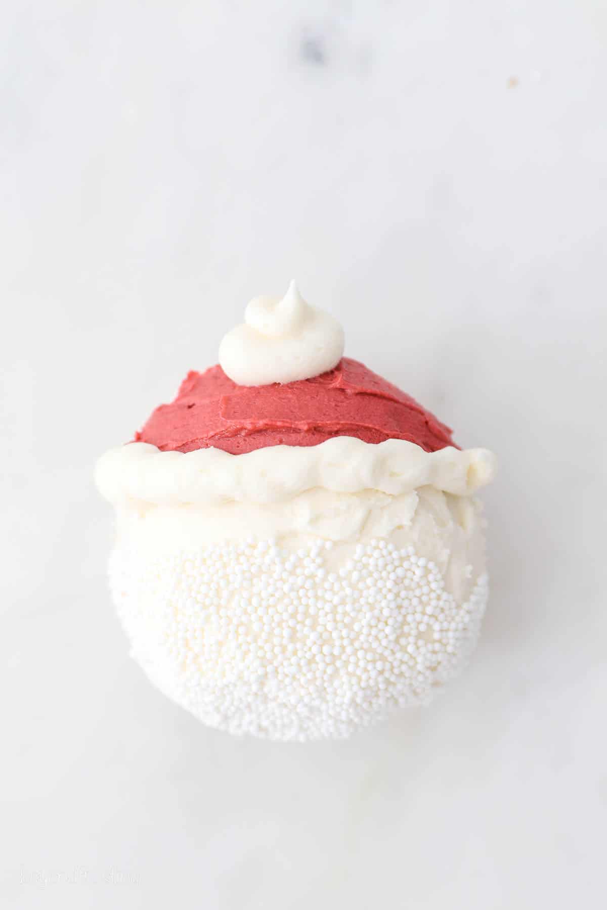 Overhead view of a cupcake partially frosted to look like Santa with a red buttercream hat and a sprinkle beard.