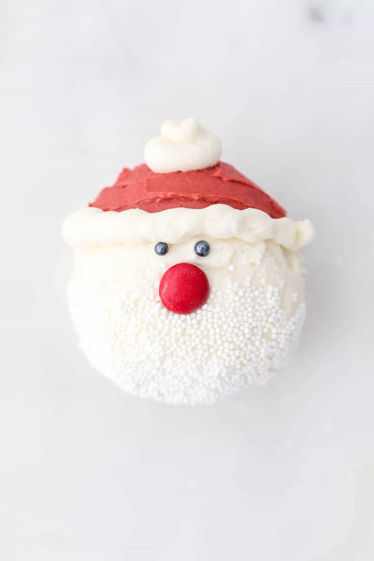 Overhead view of a cupcake frosted to look like Santa with a red buttercream hat and a sprinkle beard.