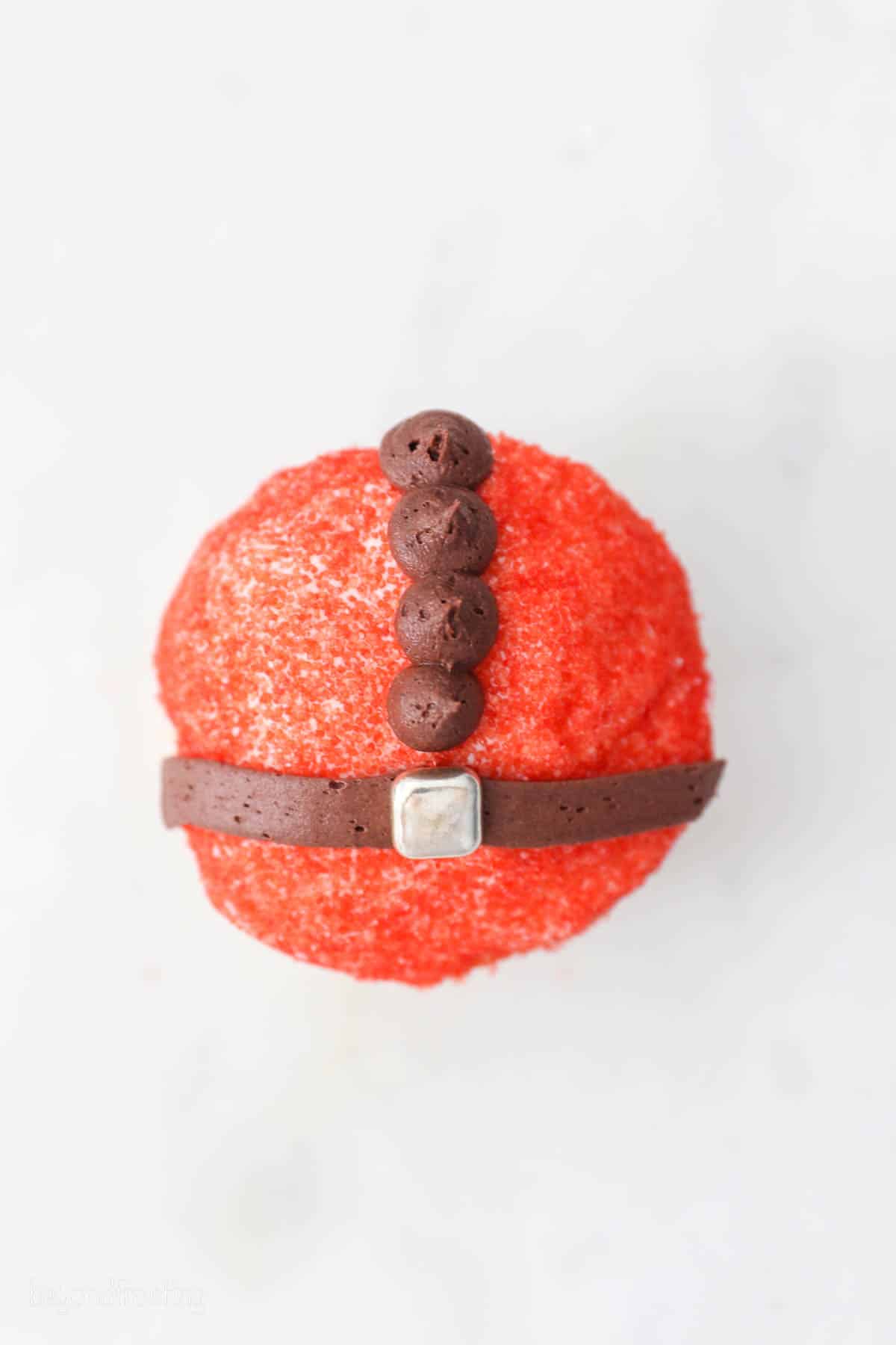 Overhead view of a cupcake decorated to look like Santa's red suit, with a brown frosting belt and buttons.