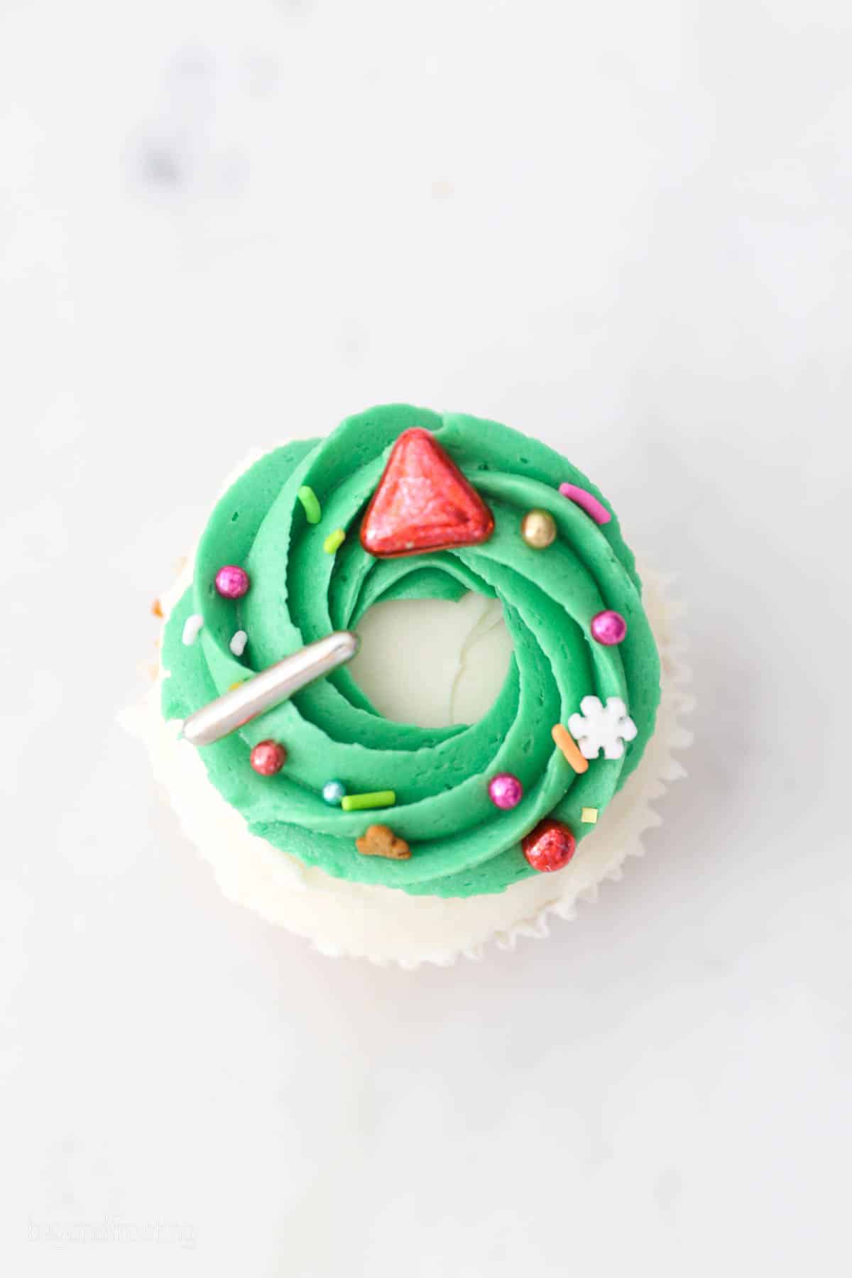 Overhead view of a Christmas cupcake decorated with a buttercream wreath and sprinkles.