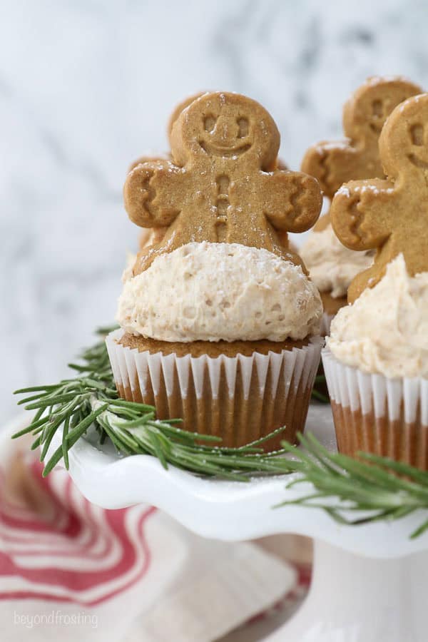 A white cake stand with gingerbread man on top of a frosted cupcakes