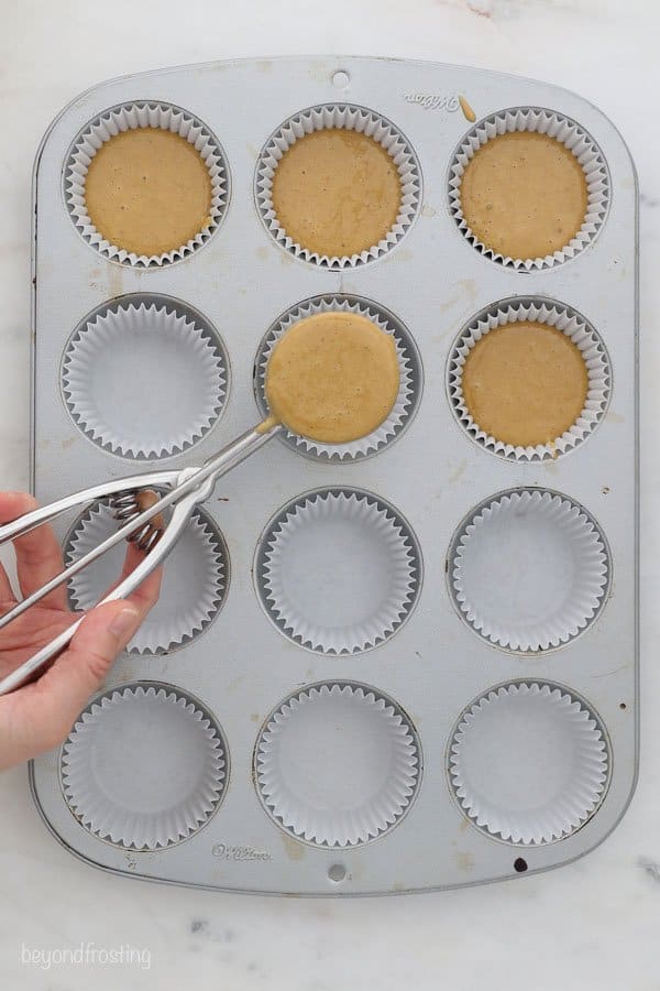 a cookie scoop with cupcake batter over top of a cupcake pan