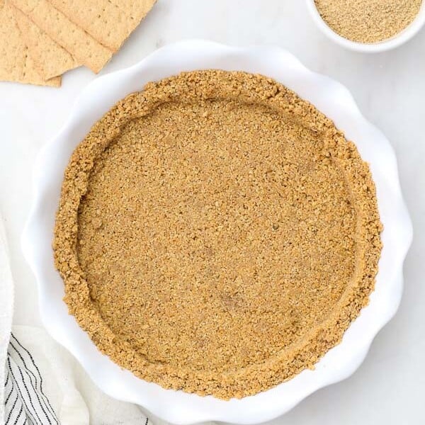 an overhead shot of a white pie plate with graham cracker crust in it