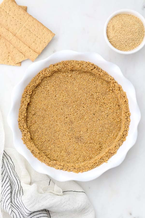 an overhead shot of a white pie plate with graham cracker crust in it