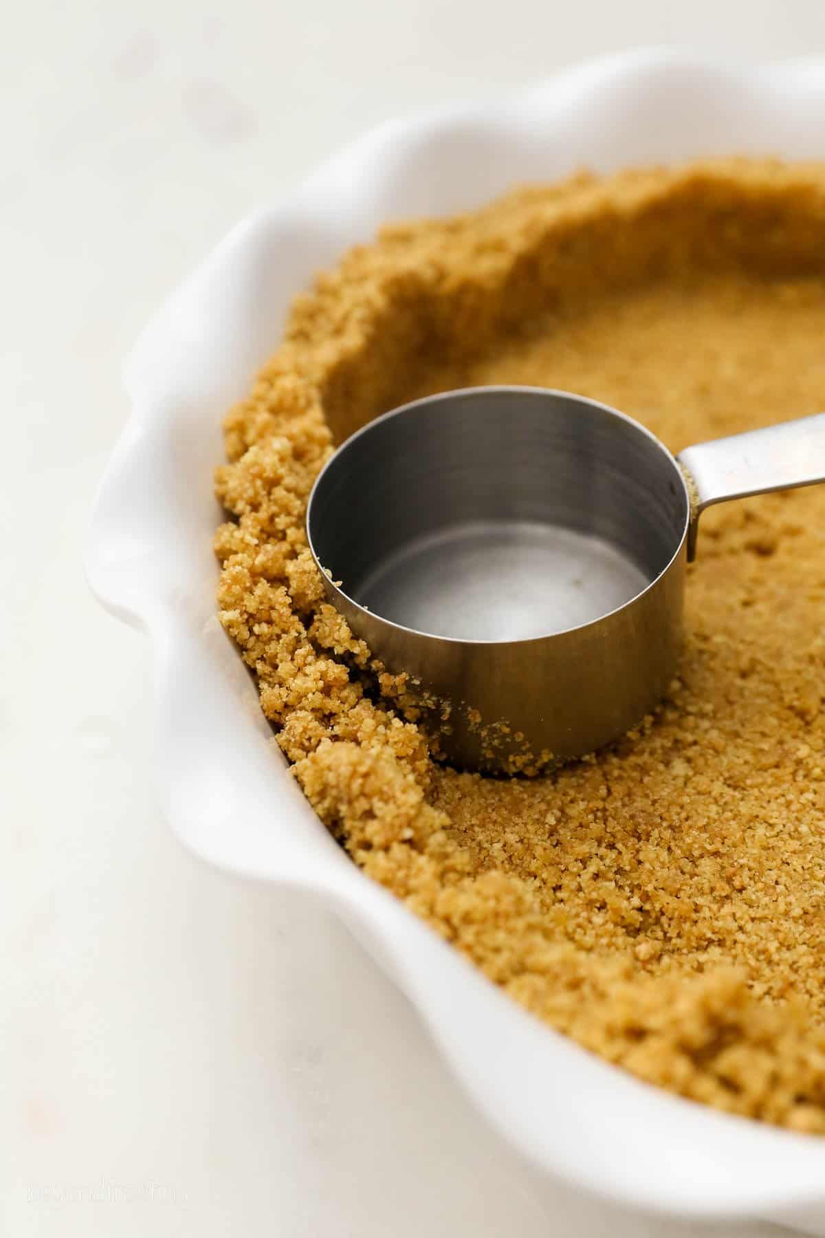 A measuring cup pressing graham cracker crust into a pie pan