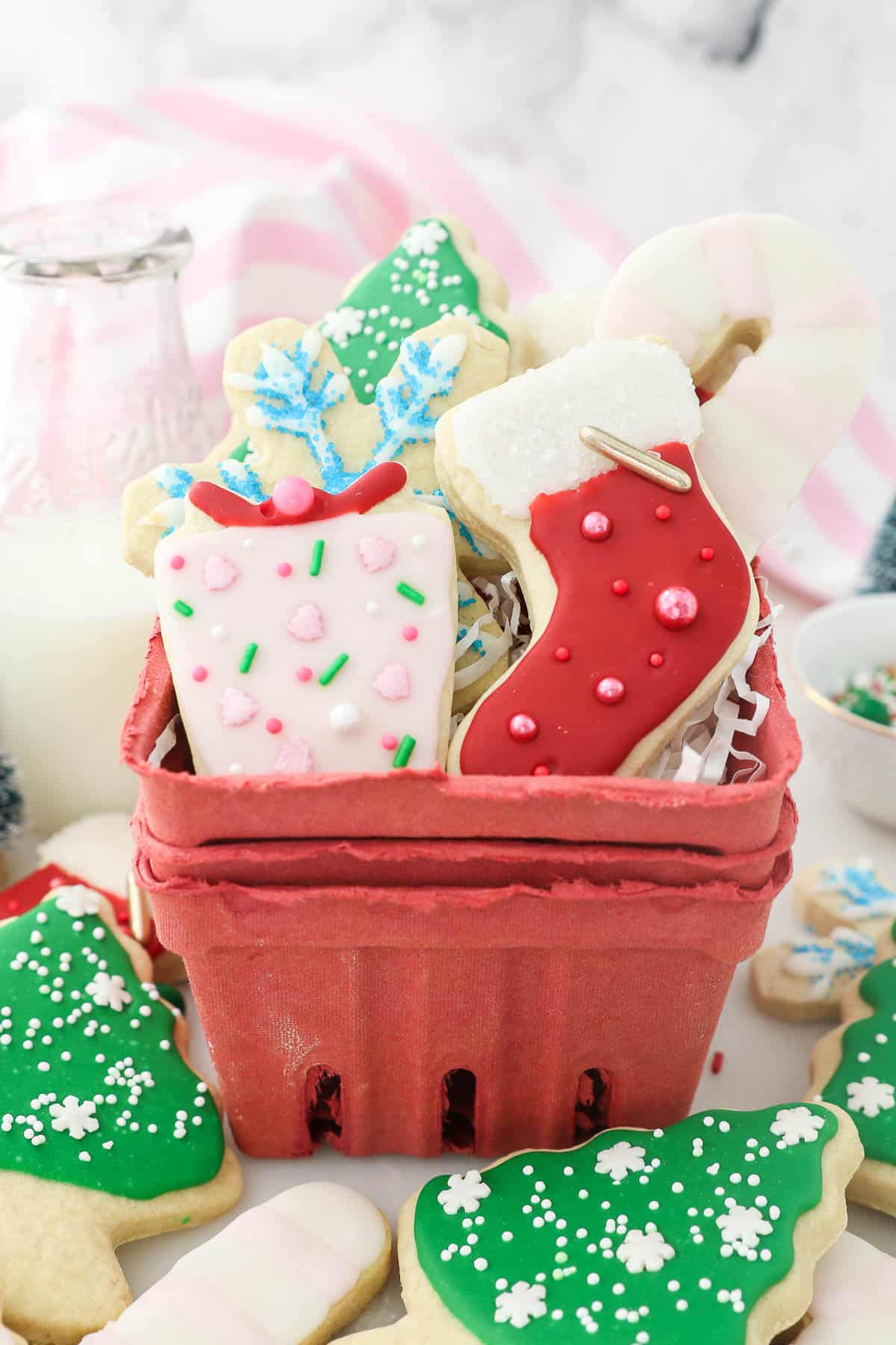 A red basket filled with assorted Christmas cut-out sugar cookies decorated with sugar cookie icing.