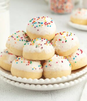 A plate of stacked anise cookies decorated with icing and nonpareil sprinkles.