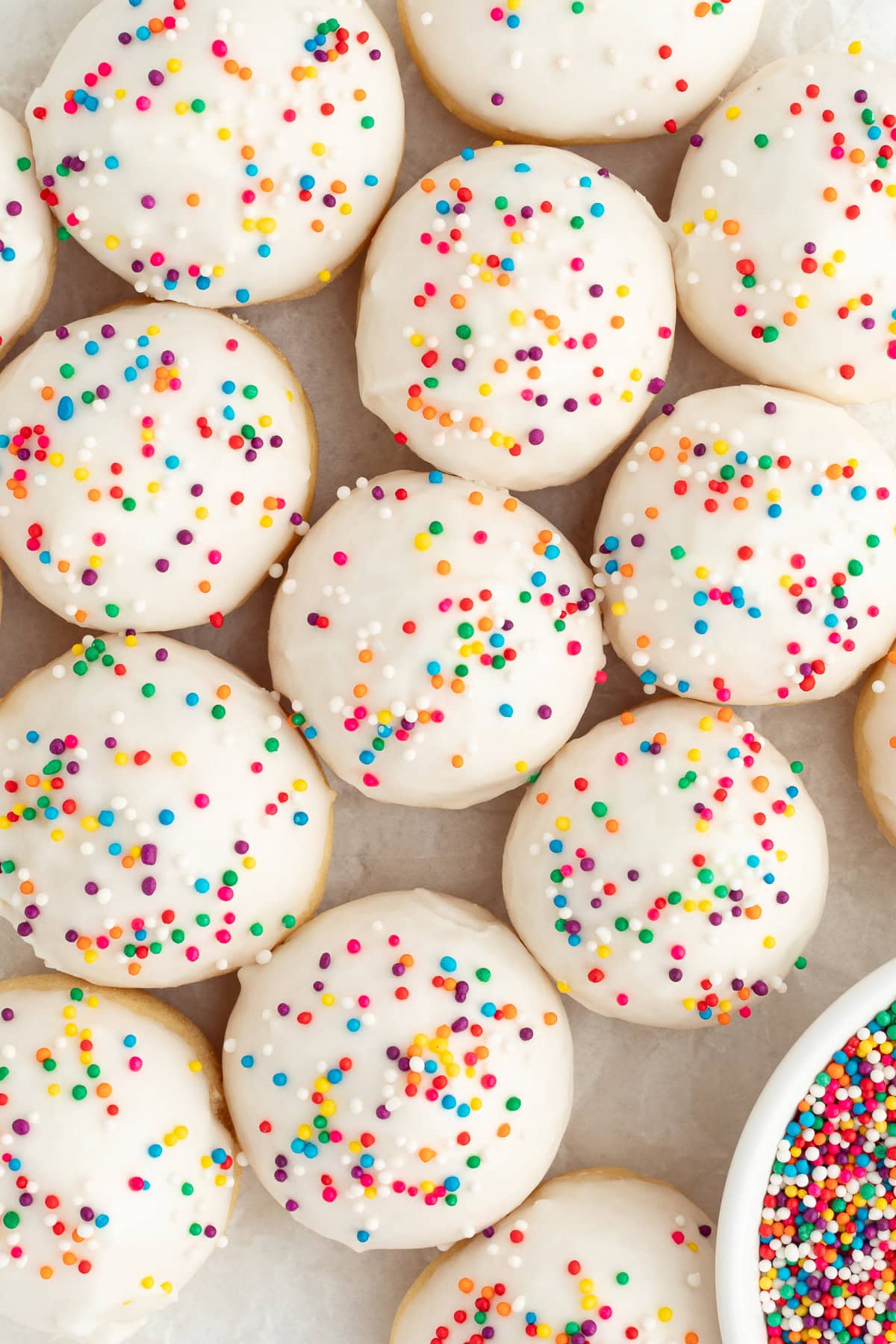 Italian anise cookies are traditional, cake-like Christmas cookies dipped in glaze and topped with sprinkles. Perfect for cookie platters! Overhead view of anise cookies decorated with icing and nonpareil sprinkles.