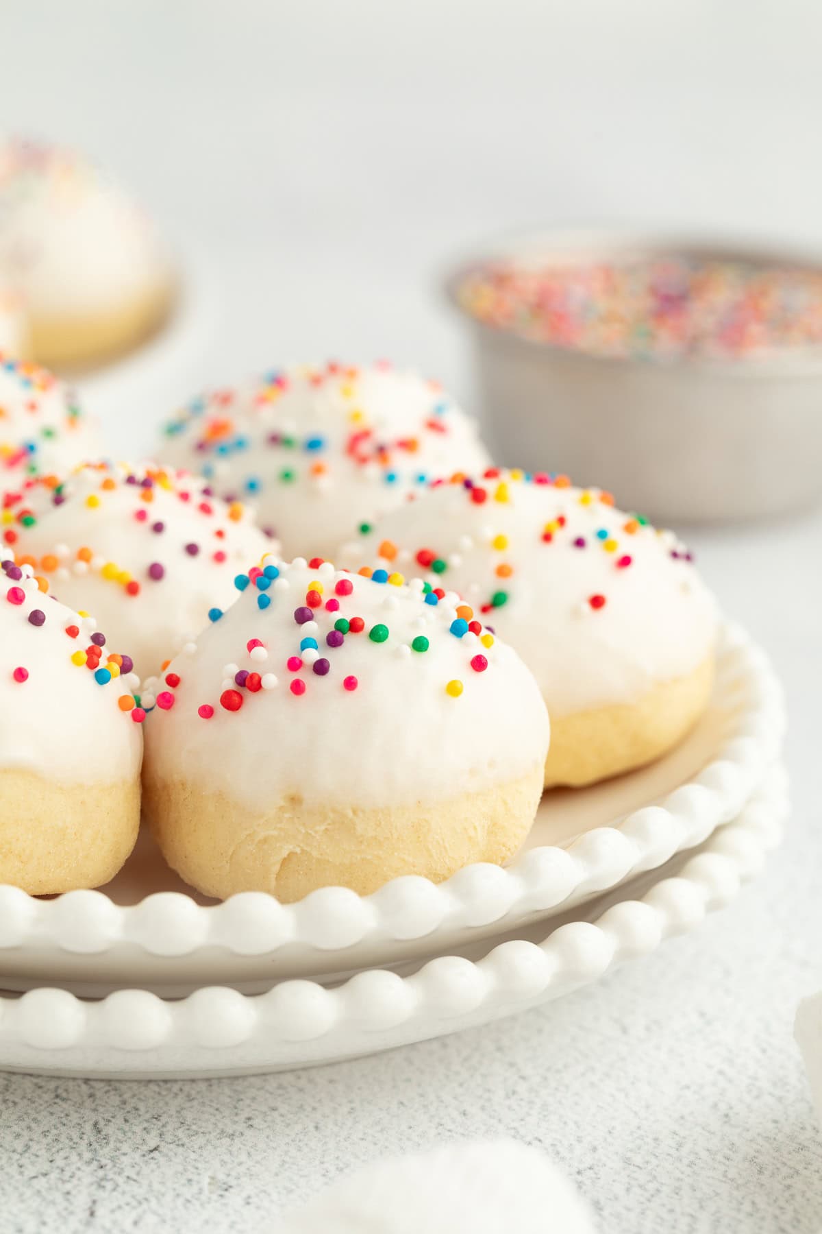 Italian anise cookies are traditional, cake-like Christmas cookies dipped in glaze and topped with sprinkles. Perfect for cookie platters! A plate of anise cookies decorated with icing and nonpareil sprinkles.