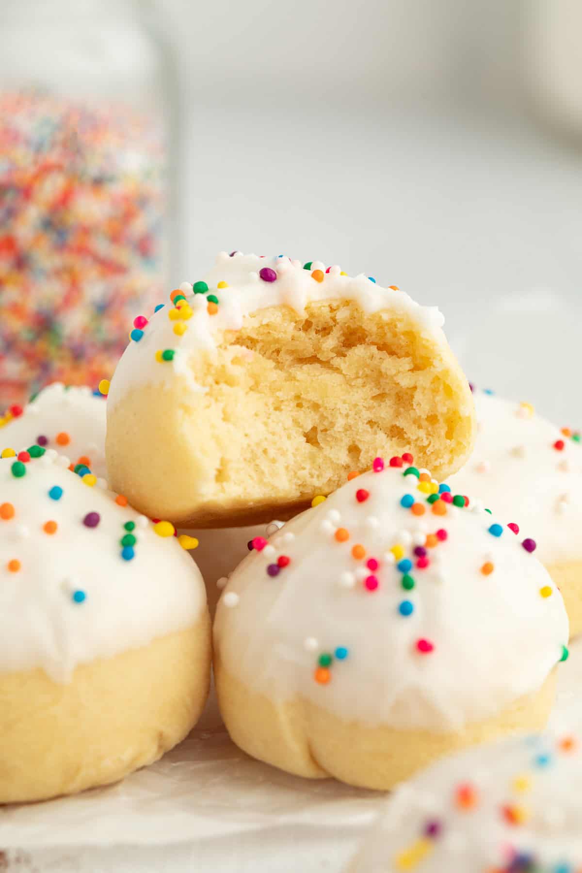 Italian anise cookies are traditional, cake-like Christmas cookies dipped in glaze and topped with sprinkles. Perfect for cookie platters! Close up of an anise cookie with a bite missing stacked on top of two more cookies.