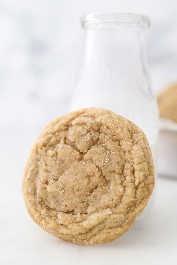 A cookie leaning up against a glass of milk