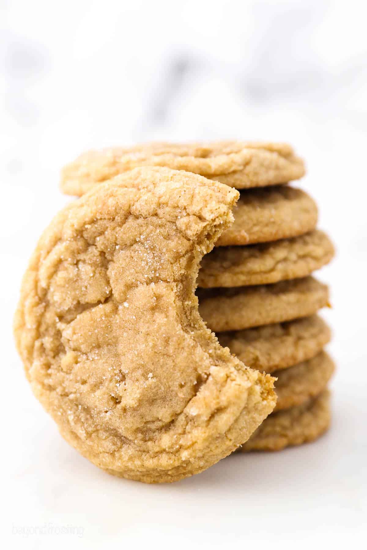 A brown sugar cookie with a bite missing leaning against a tall stack of sugar cookies.