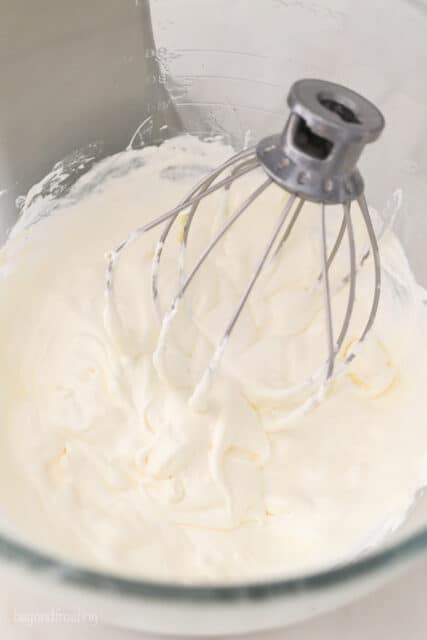 overhead view into a glass mixing bowl with frosting and whisk attachment
