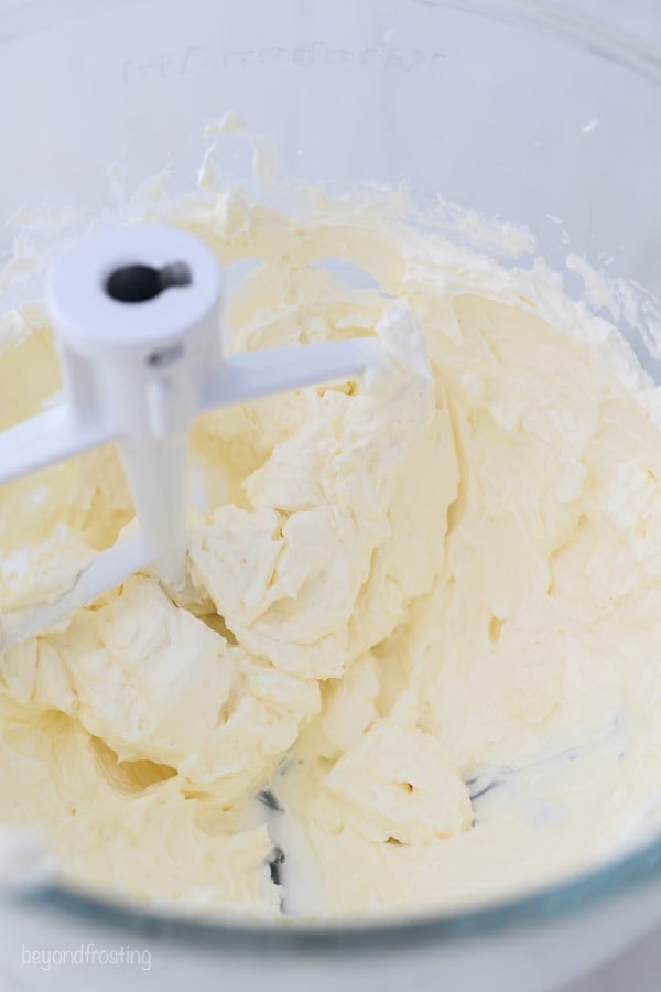 overhead view into a glass mixing bowl with frosting and mixer attachment