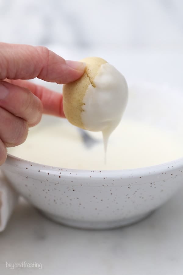 a hand dipping a cookie in a vanilla glaze