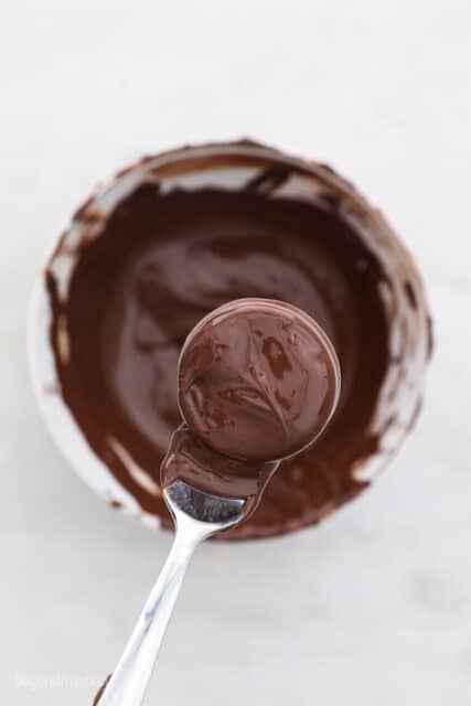 A fork with a chocolate covered Oreo hanging over a bowl a melting chocolate