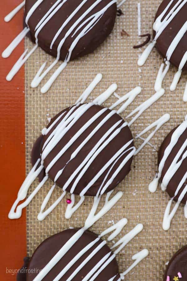 A chocolate covered Oreo drizzled with white chocolate on a silicone baking mat