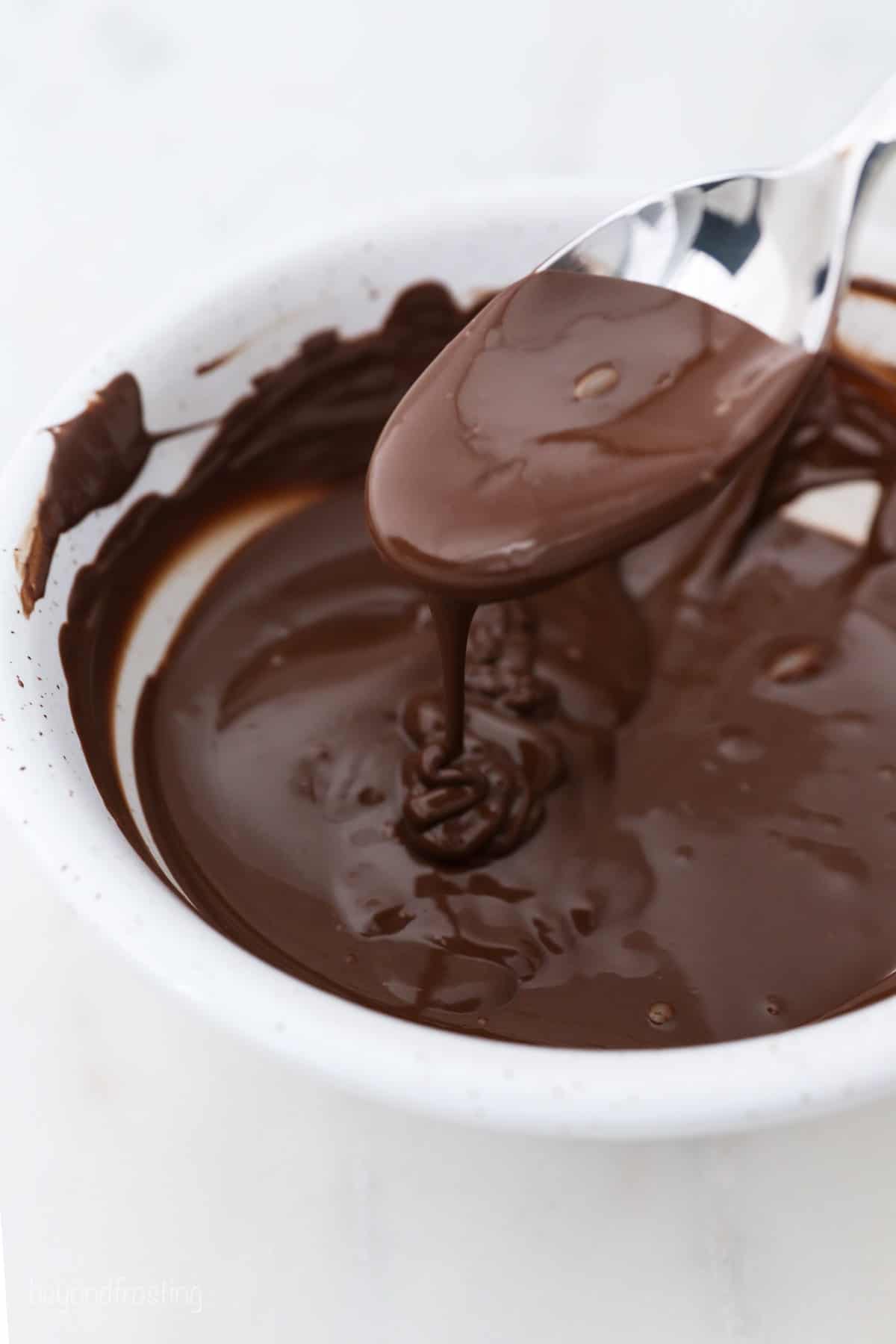 A spoon drizzling melted chocolate into a white bowl.