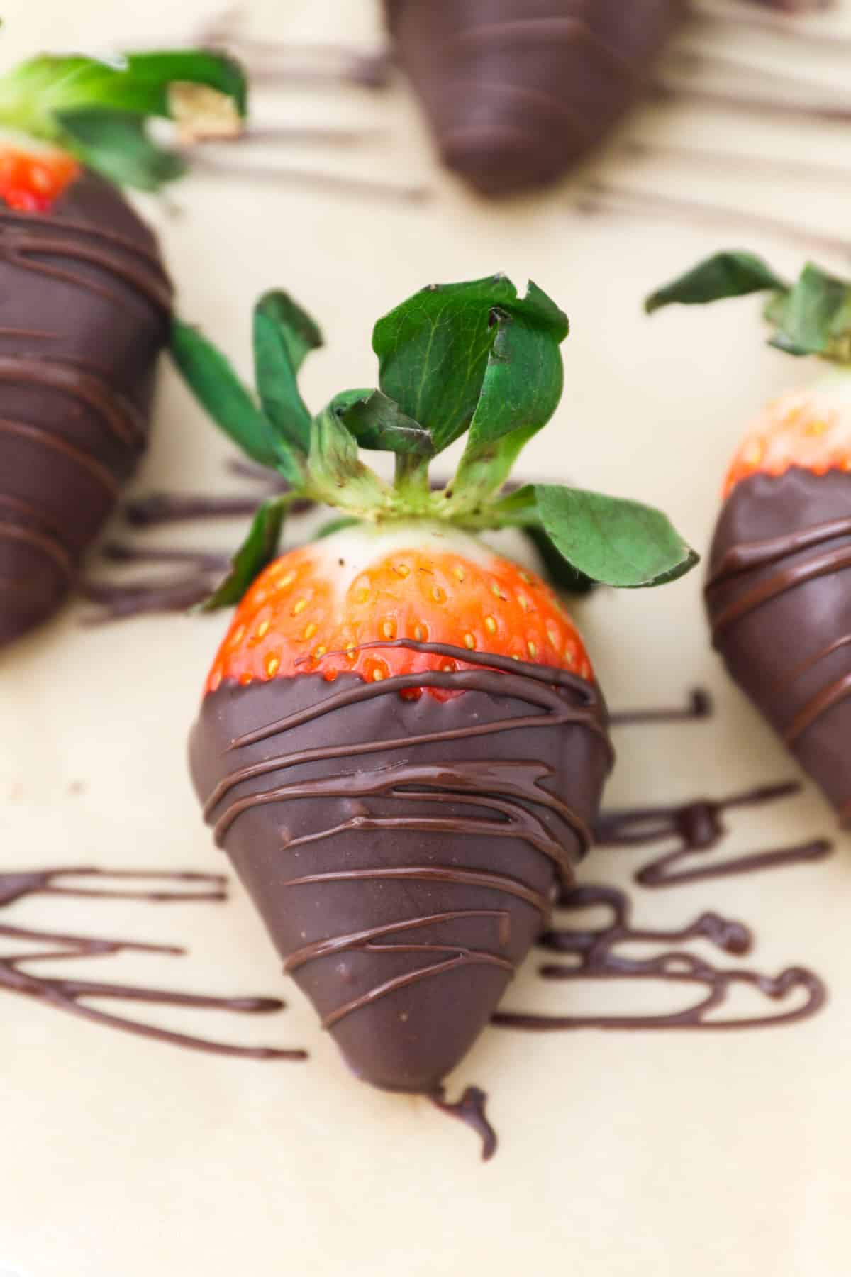A chocolate covered strawberry on a lined baking sheet, drizzled with chocolate.