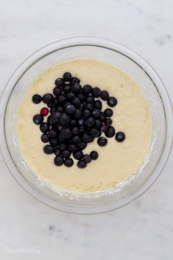 an overhead shot of a glass mixing bowl of muffin batter with fresh blueberries